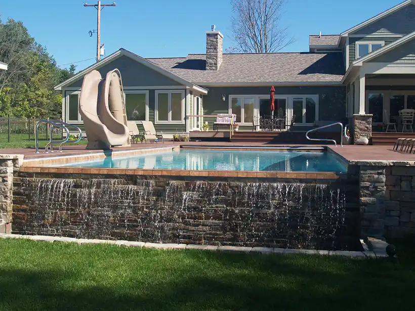 Raised wall pool spilling a waterfall over fieldstone, house behind