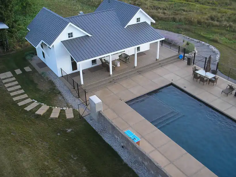 Aerial view of a white farmhouse with its pool and patio