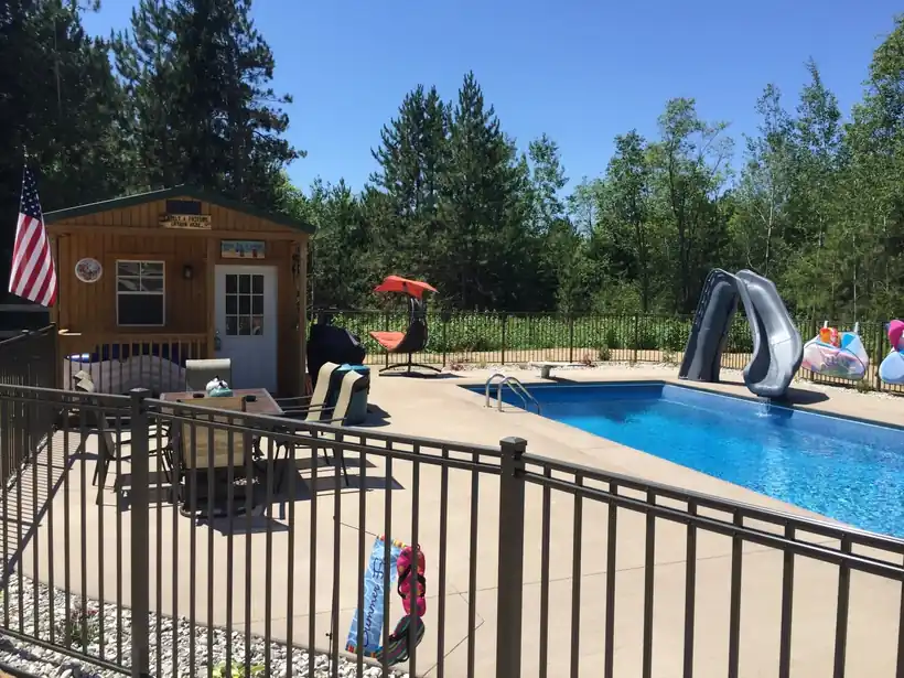 Pool with a slide behind an iron fence, a cabin beyond