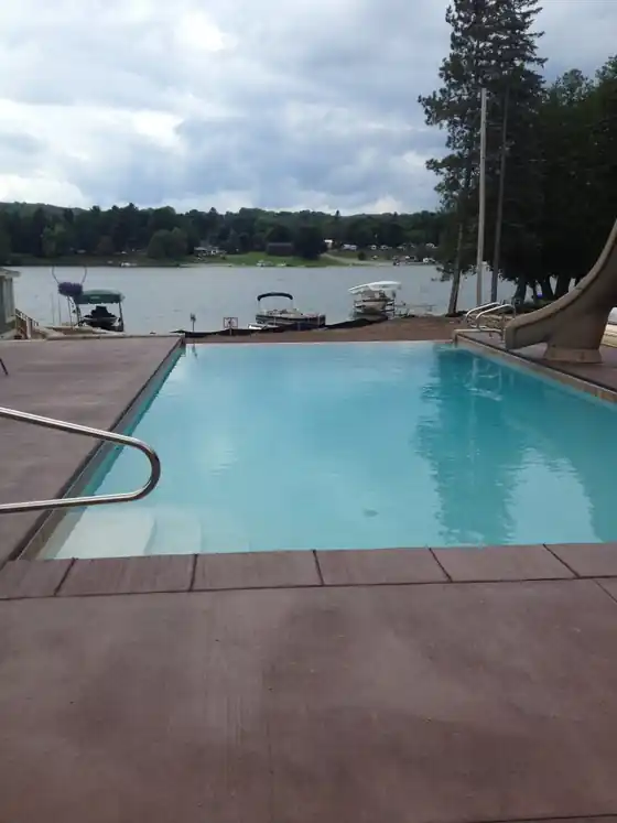A finished rectangular pool with a red concrete deck beside the lake